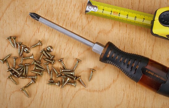 Screws and screwdriver on wooden background.