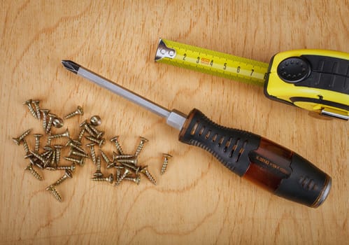 Screws and screwdriver on wooden background.