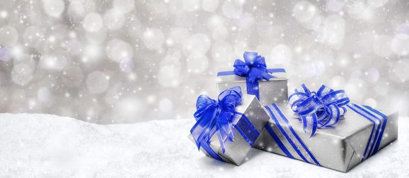 Silver Christmas or birthday gift boxes with red bows in snow,with snowy night background,panorama format
