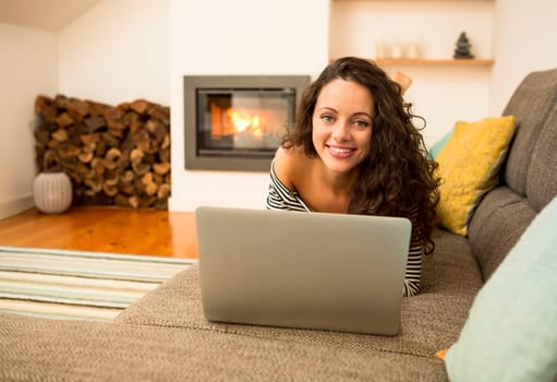 Beautiful woman working with a laptop at the warmth of the fireplace