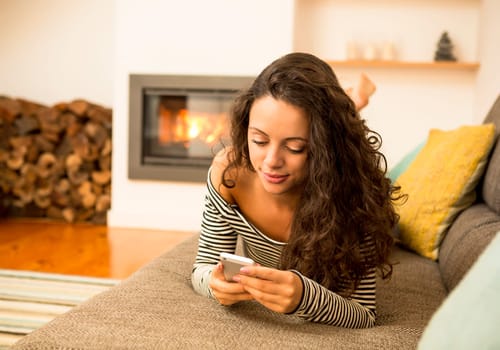 Beautiful woman using a cellphone at home at the warmth of a fireplace