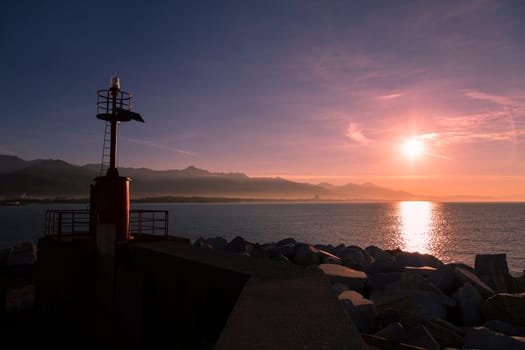 Costal landscape with lighthouse in backlight and the mountain range in the background