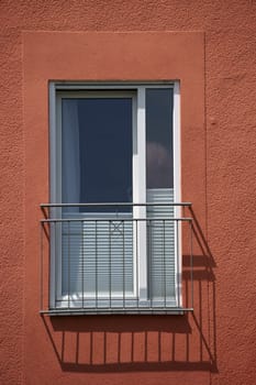 A railing in front of a window of a residential building casts a shadow.