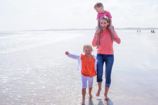 Young single mother at the beach with her son and daughter. They are laughing and are barefoot in the water.