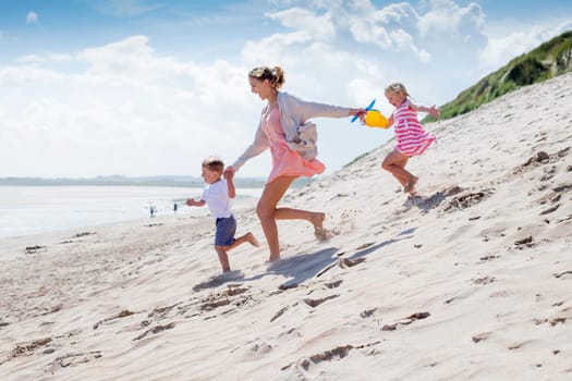 Young single parent family holding hands and running down the sanddunes to the sea. They are laughing and wearing casual clothing.