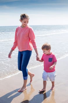 Young mother and son walking along the beach. They are looking at each other and smiling.