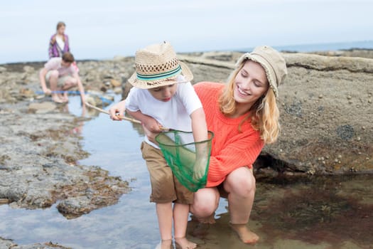 Young family searching for crabs among the rocks at the seaside. The young boy is reaching into his net for a crab and his mother is looking at him and smiling.