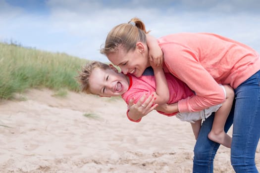 Young mother and son at the beach. She is holding him and they are both laughing.