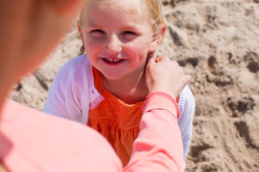 Young girl at the beach looking up at her mother and smiling.
