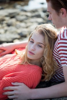 Portrait of a beautiful couple lying on a rock at the beach. They look very content and happy together.