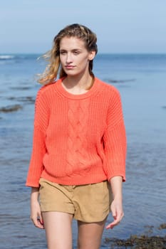 Portrait of a beautiful young woman at the beach. She is looking at the camera and wearing casual clothing while standing in the sea.