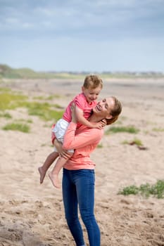 Young mother and her son on the beach. She is holding the little boy and they are both smiling.