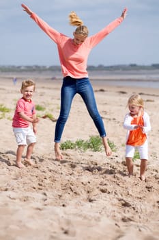 Beautiful little family playing together at the beach. The mother is jumping in the air while her children play around her.