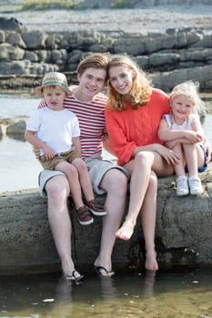 Portrait of a beautiful young family at the beach. They are wearing casual clothing and smiling at the camera.
