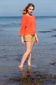 Portrait of a beautiful young woman at the beach. She is looking at the camera and wearing casual clothing while standing in the sea.