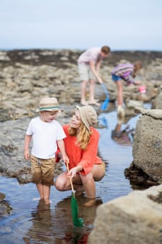 Young family at the beach searching for creatures in the rock pools. They are wearing casual clothing and holding fishing rods.