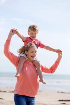 Portrait of a young mother and son at the beach together. They are both smiling and the little boy is on his mothers shoulders.