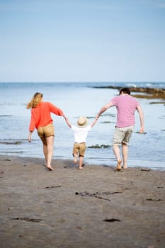 Young two parent family at the beach with their young son. They are all holding hands and swinging the little boy.