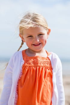 Portrait of a beautiful little girl outdoors. She is wearing casual clothing and smiling at the camera.