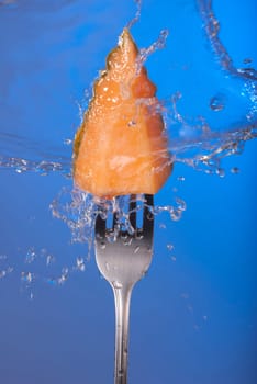 Melon fruit piece on fork with water splash and empty blue background concept photo. Ideal for healthy eating campaign, motivation or fitness poster.   .
