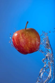 Delicious organic red apple fruit on blue background with water splash motion. Ideal for health campaign or poster.