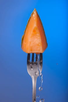 Melon fruit piece on fork with water splash and empty blue background concept photo. Ideal for healthy eating campaign, motivation or fitness poster.   .
