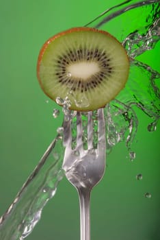 Kiwi fruit on fork with water splash and color background, concept photo. Ideal for healthy eating campaign or fitness poster.