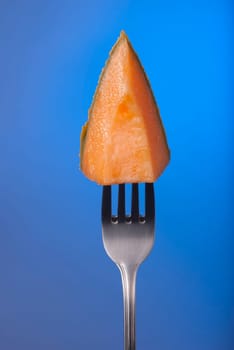 Melon fruit piece on fork with empty blue background concept photo. Ideal for healthy eating campaign, motivation or fitness poster.