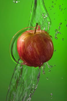 Delicious organic red apple fruit on green background with water splash motion. Ideal for health campaign or poster.