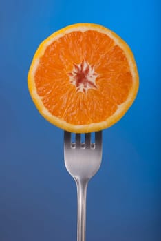 Delicious orange fruit cut in half on fork with blue color background concept photo. Ideal for healthy eating campaign or fitness poster.