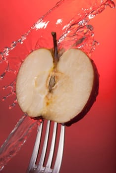 Red apple cut in half on fork with water splash, color background concept photo. Ideal for healthy eating campaign or fitness poster.