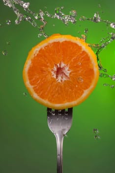 Delicious orange fruit cut in half on fork with water splash, green color background. Ideal for healthy diet eating campaign or fitness poster.