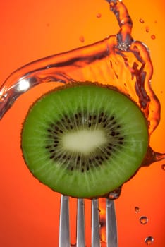 Close up of kiwi fruit center on fork with water splash and color background, concept photo. Ideal for healthy eating campaign or fitness poster.