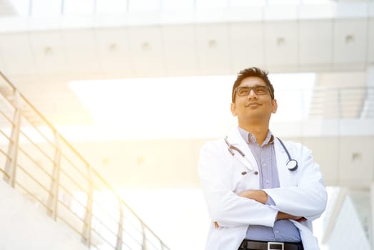 Portrait of confident Asian Indian medical doctor standing outside hospital building, beautiful golden sunlight at background.