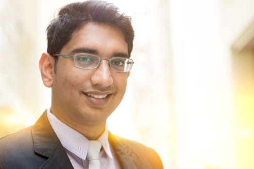 Close up portrait of handsome Asian Indian business man smiling, outside modern office building block, beautiful golden sunlight at background.