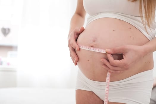 Young new mother is measuring her size of her belly