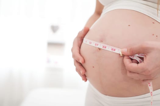 Young new mother is measuring her size of her belly