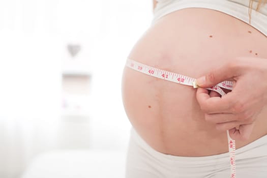 Young new mother is measuring her size of her belly