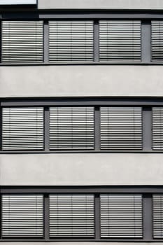 The modern facade of an office building with a series of windows and metallic blinds