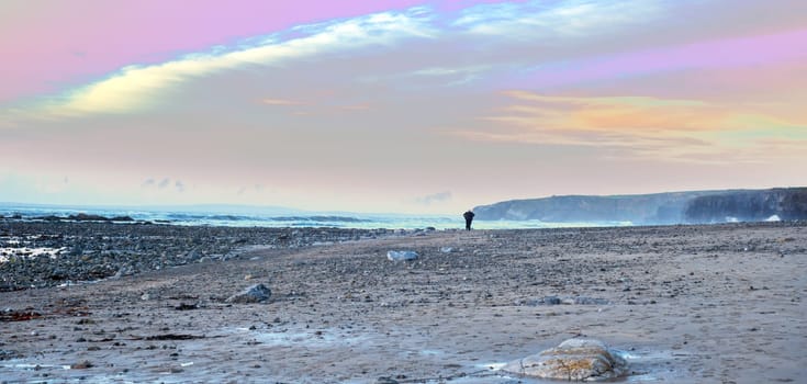 man walking at rocky beach near ballybunion on the wild atlantic way ireland with a beautiful yellow sunset