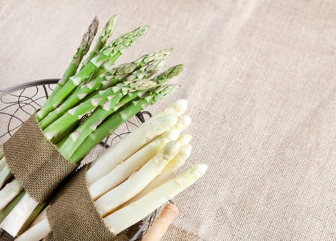 fresh green and white asparagus bundled in a basket with a cloth ribbon