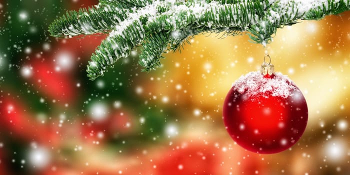 Red Christmas bauble in snow hanging from a fir branch,with colorful blurred background