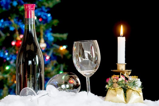 Bottle and two glasses of wine on the snow in front of a Christmas tree