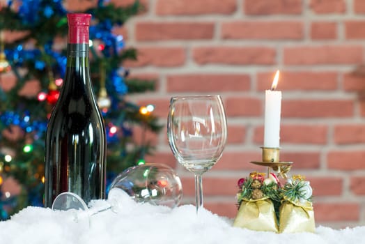 Bottle and two glasses of wine on the snow in front of a Christmas tree