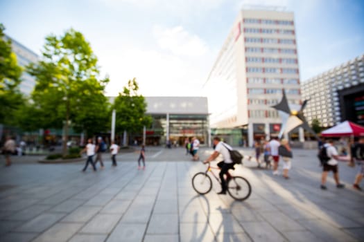 Out of focus street scene from a city center in summer, pedestrians walking and cycling