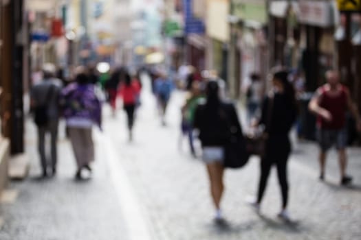 Out of focus shot af a busy shopping street, shoppers walking up and down the street