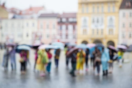 Out of focus shot of a group of people standing with umbrellas in the rain, buildings in the background