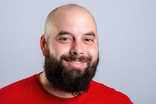 young bearded man in red shirt in front of gray background