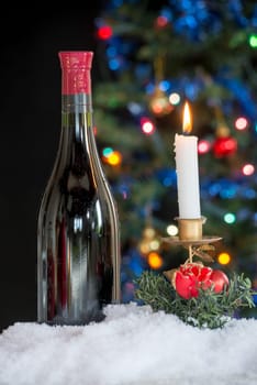a bottle of red wine and a candle with a Christmas tree in background