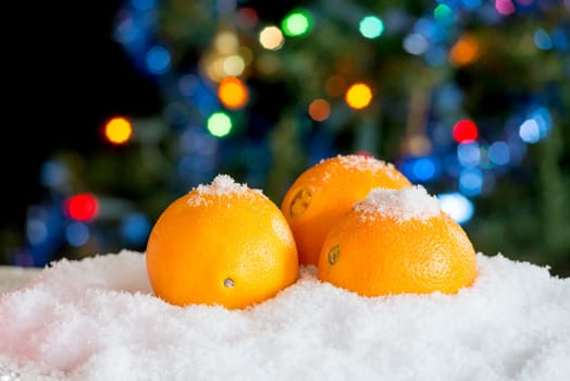 Three oranges in the snow with Christmas decor and bokeh